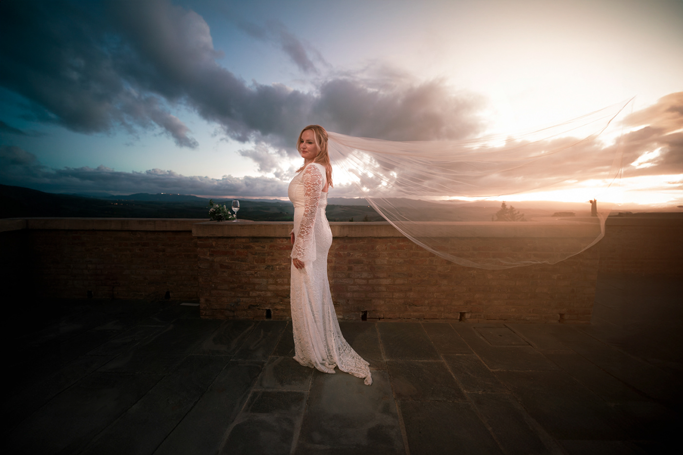 Bride with flying veil in front of the sunset in a castle terrace in italy.