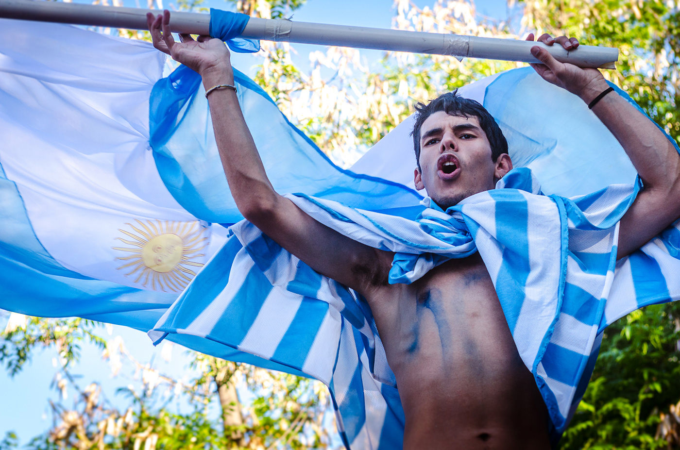 Un muchacho festejando con un estandarte con la bandera argentina y una capa de la bandera argentina