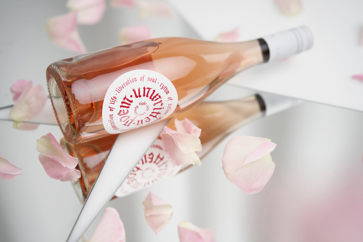 Rose petals and a bottle of sparkling rosé sparkling wine resting on a top of a table 