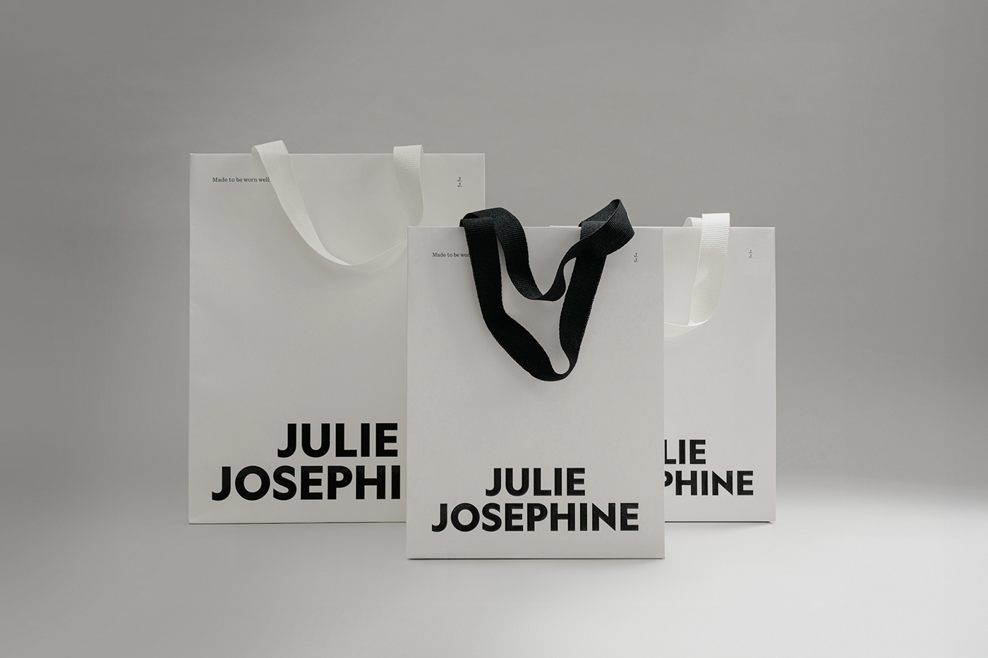 3 white paper carry bags featuring large uppercase lettering in a white space
