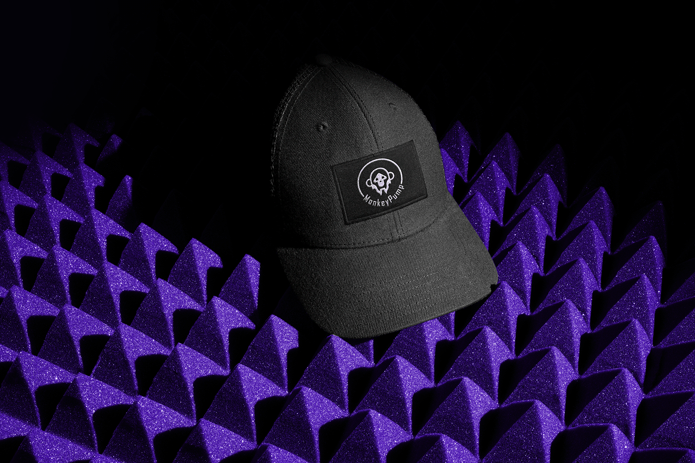 Image of a black cap with the MonkeyPump Logo on purple foam background.