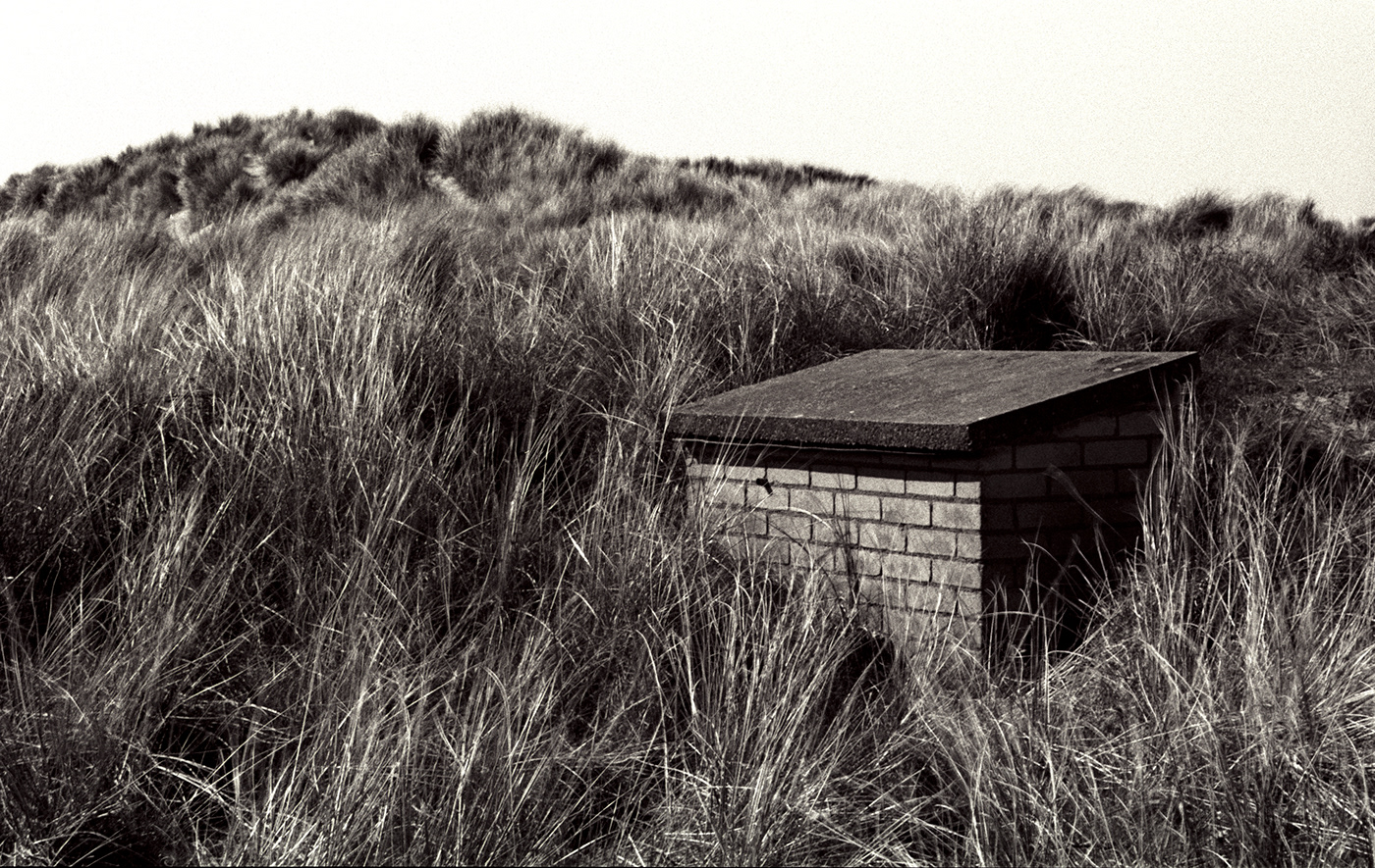 Monochrome image of a small brick bunker in dune grassland