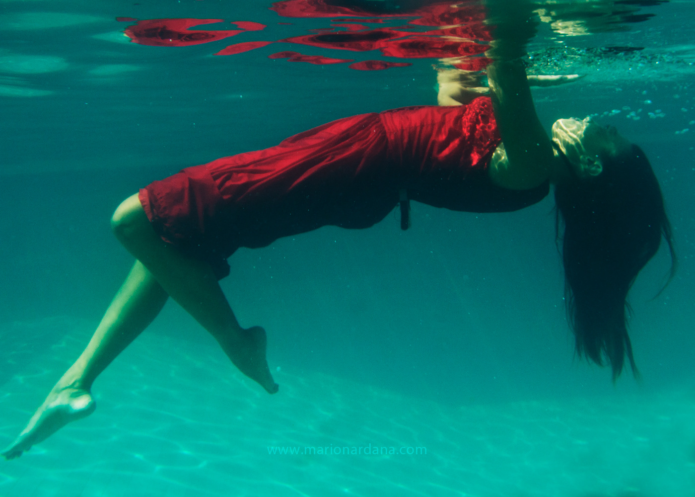 A woman is submerged in a red dress under water.