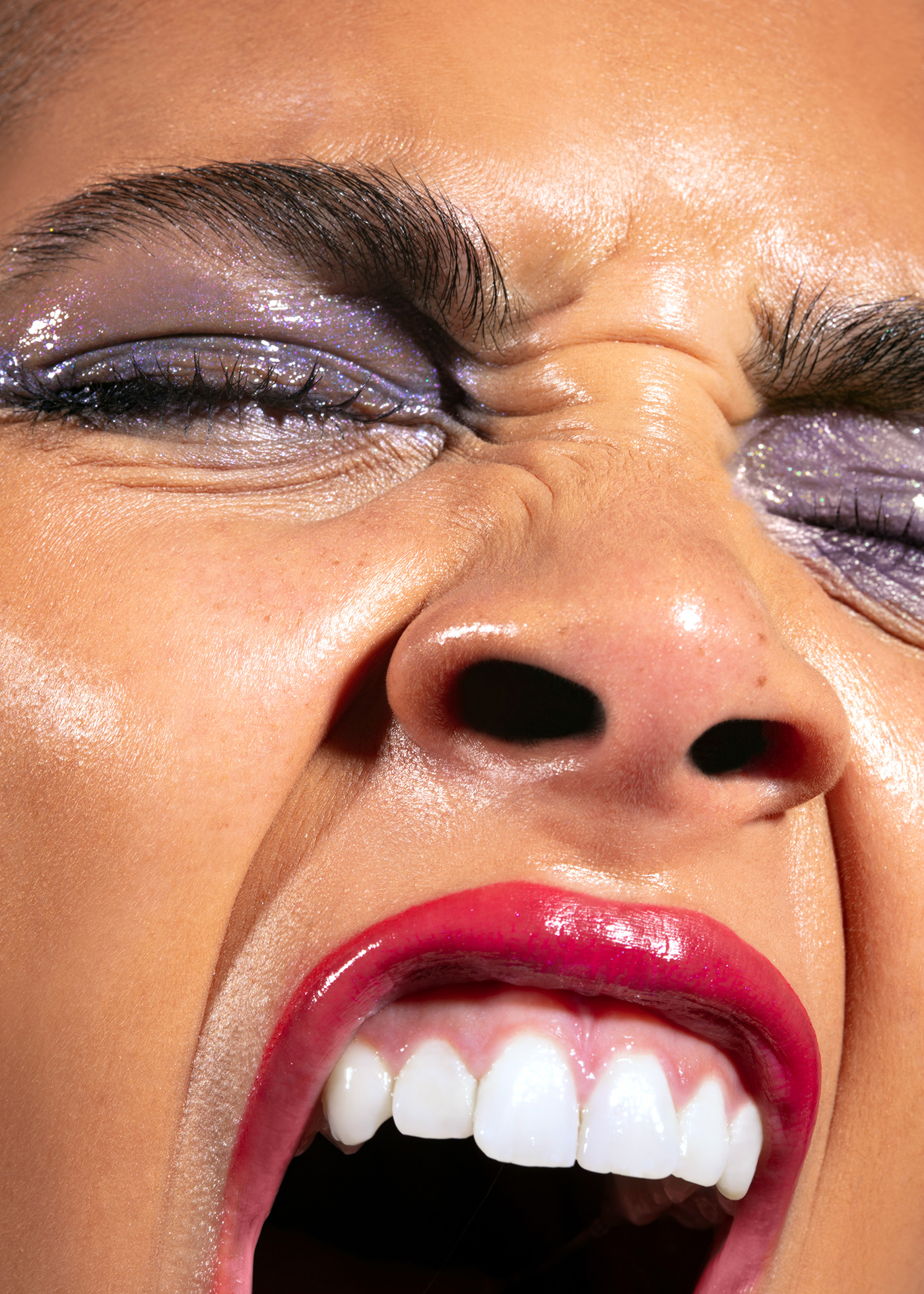 A beauty photograph of a model with glossy purple makeup, shiny skin and pink lipstick screaming 