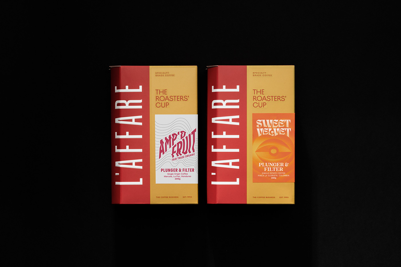 Wide shot of two red and gold coffee boxes with large typography details on a black background