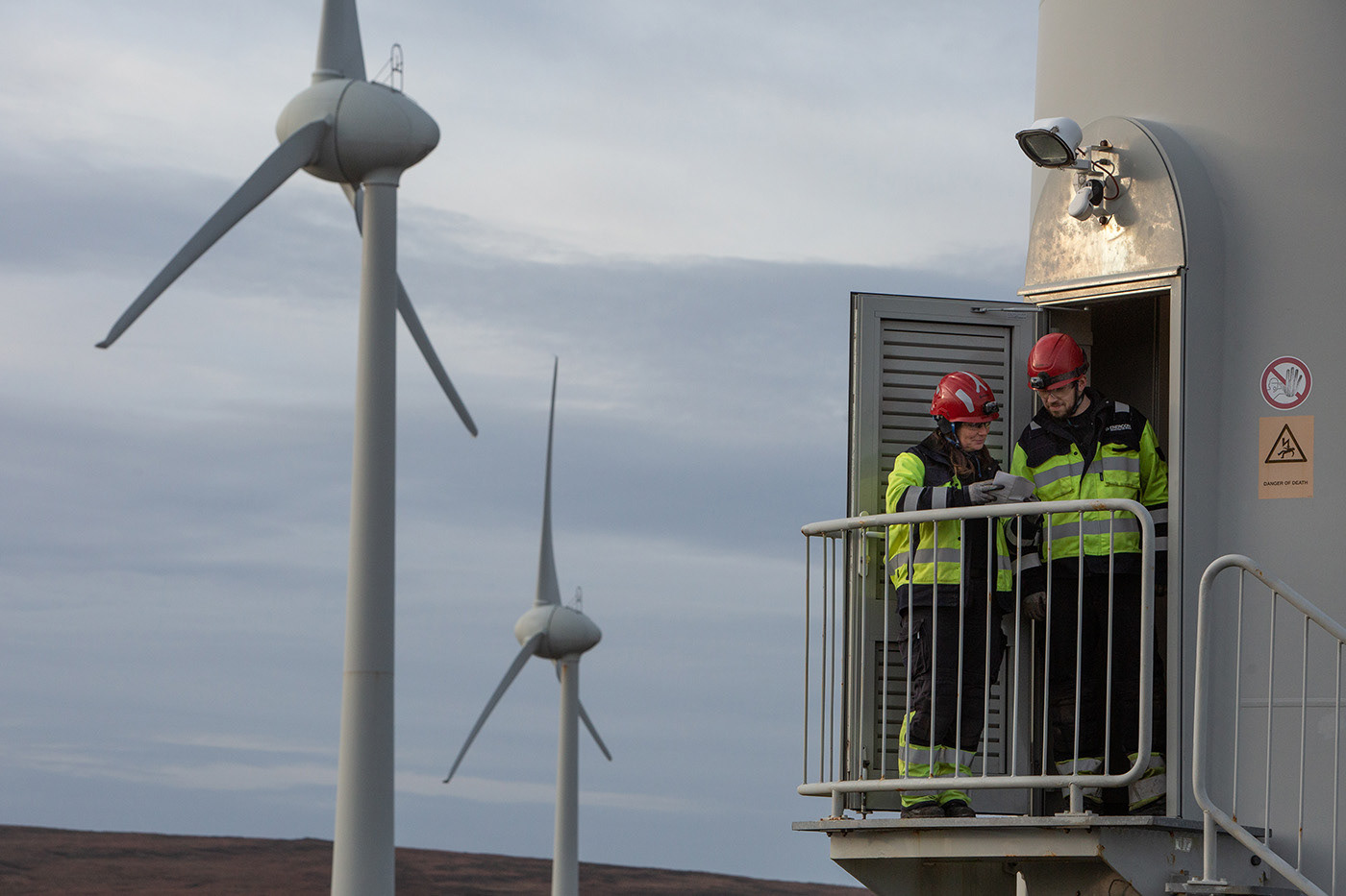 male and female worker at open door of a wind turbine, turbines in distance behind them