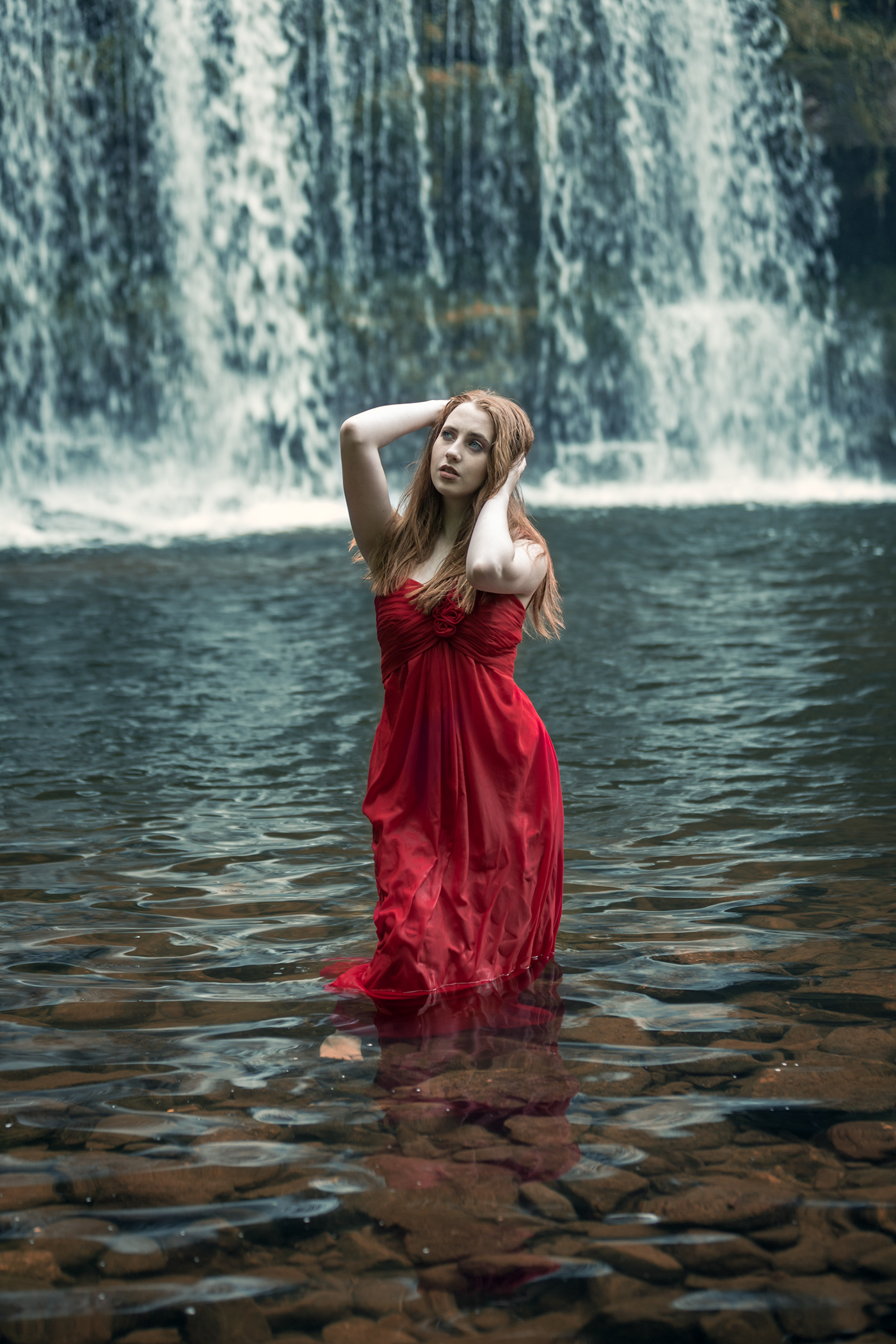 Beauty portraits in nature with the model in a red dress , in the water against a waterfall 
