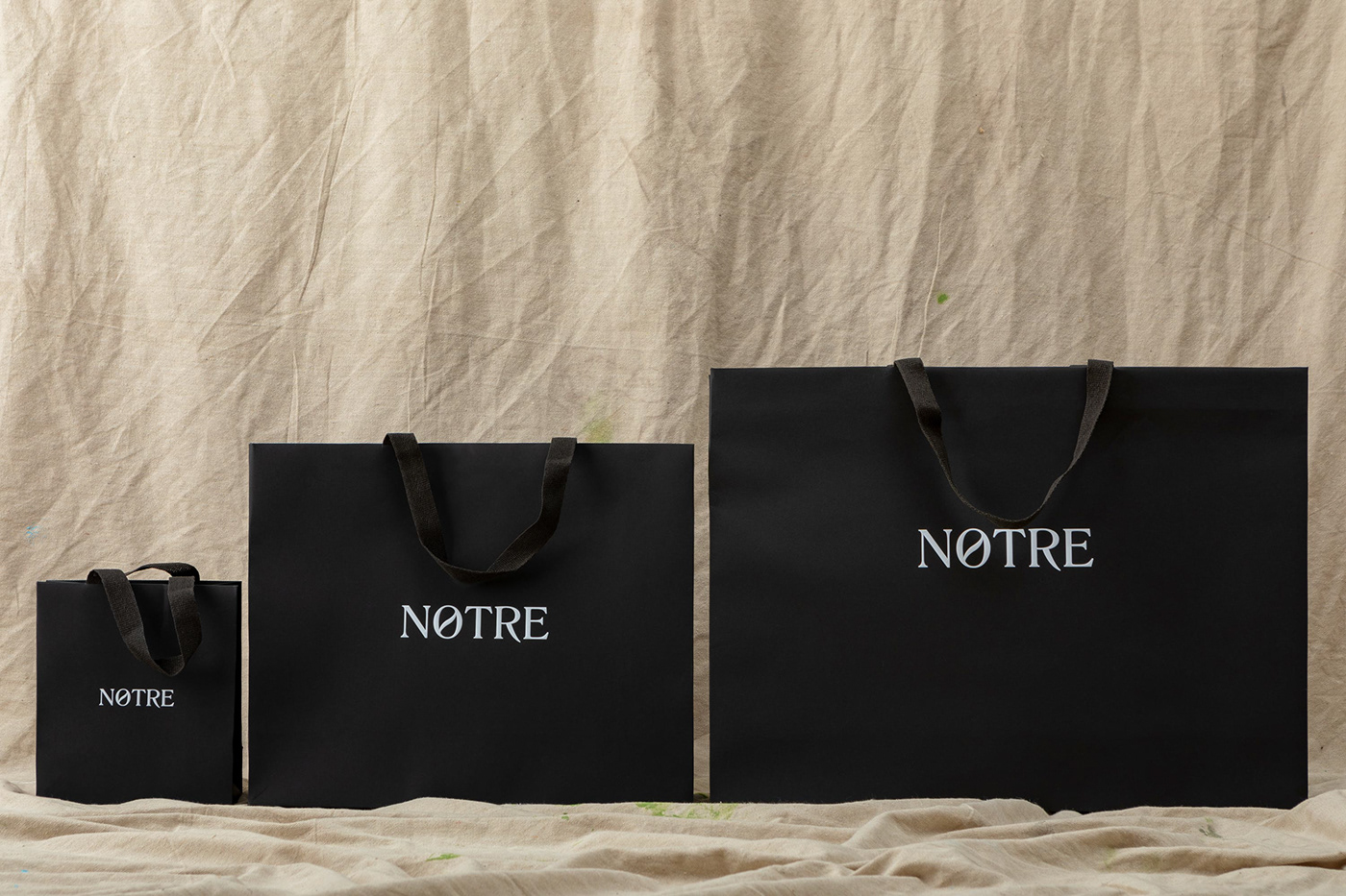 3 different sized black retail bags with white text sit on a beige drop sheet