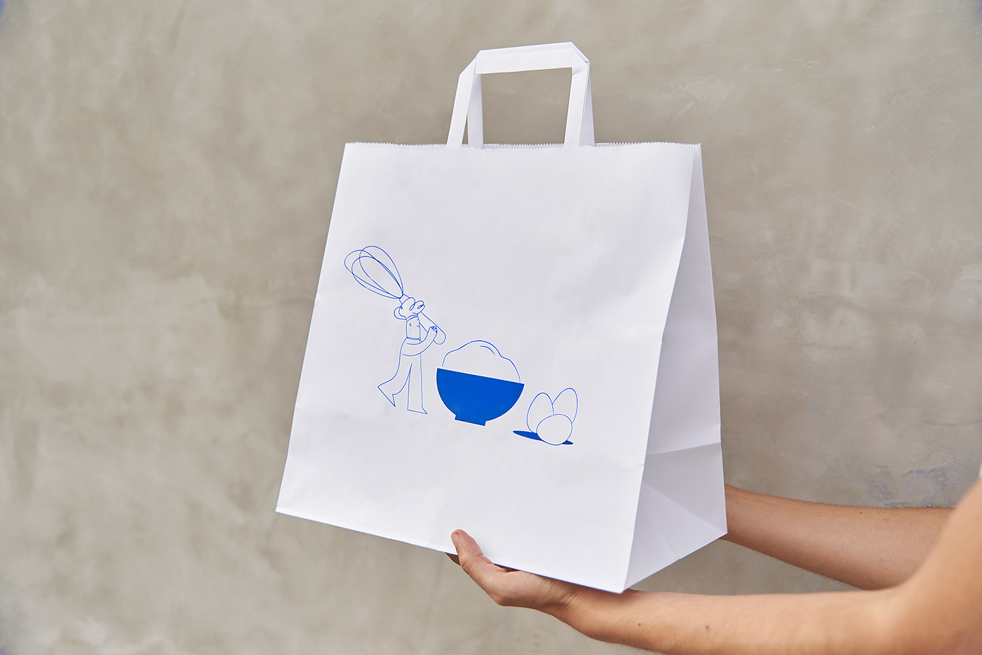 An illustration of a chef baking with eggs and flour. El idealista on a shopping bag.