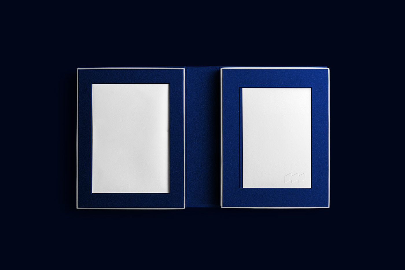 Dois livros com capas azuis e espaços em branco centrais sobre fundo escuro, logotipo discreto.
