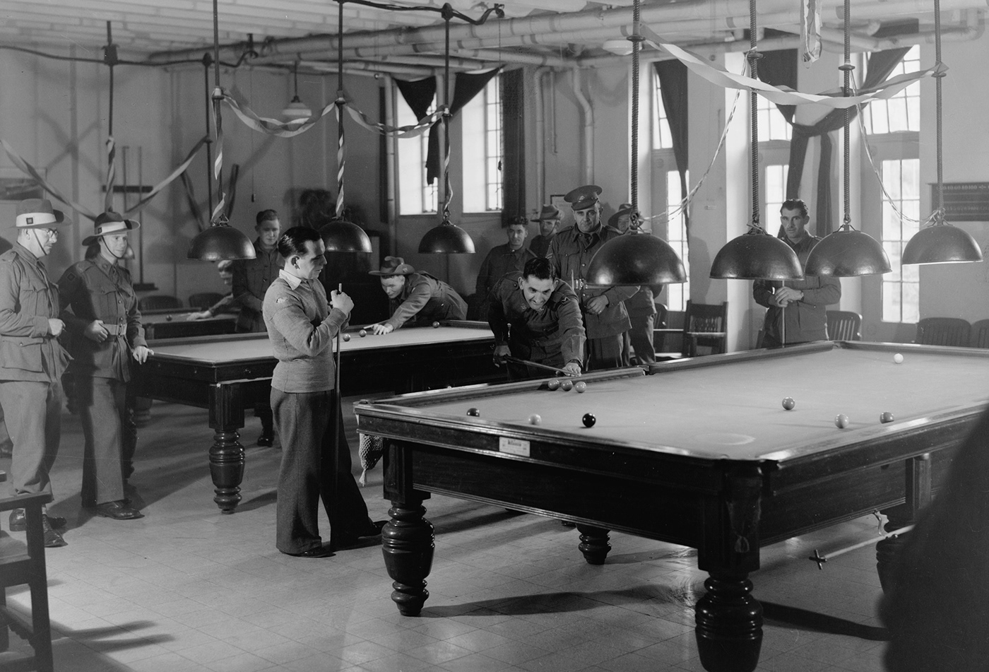 Old photo of soldiers playing billiards in a wide room with many billiards tables