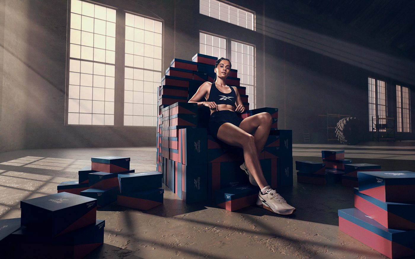 Athlete sitting atop a throne of shoe boxes in a gym, promoting Reebok footwear.
