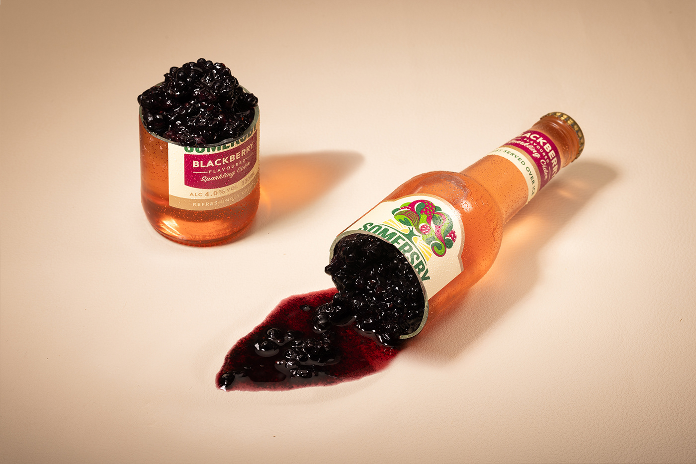 A cider bottle photographed to appear to have been "cut" opened, with crushed blackberries inside.