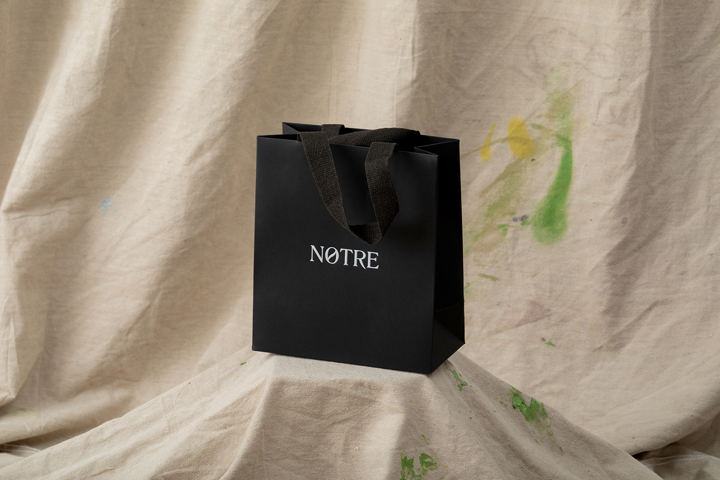 Wide shot of small black retail paper bag on a beige drop sheet background