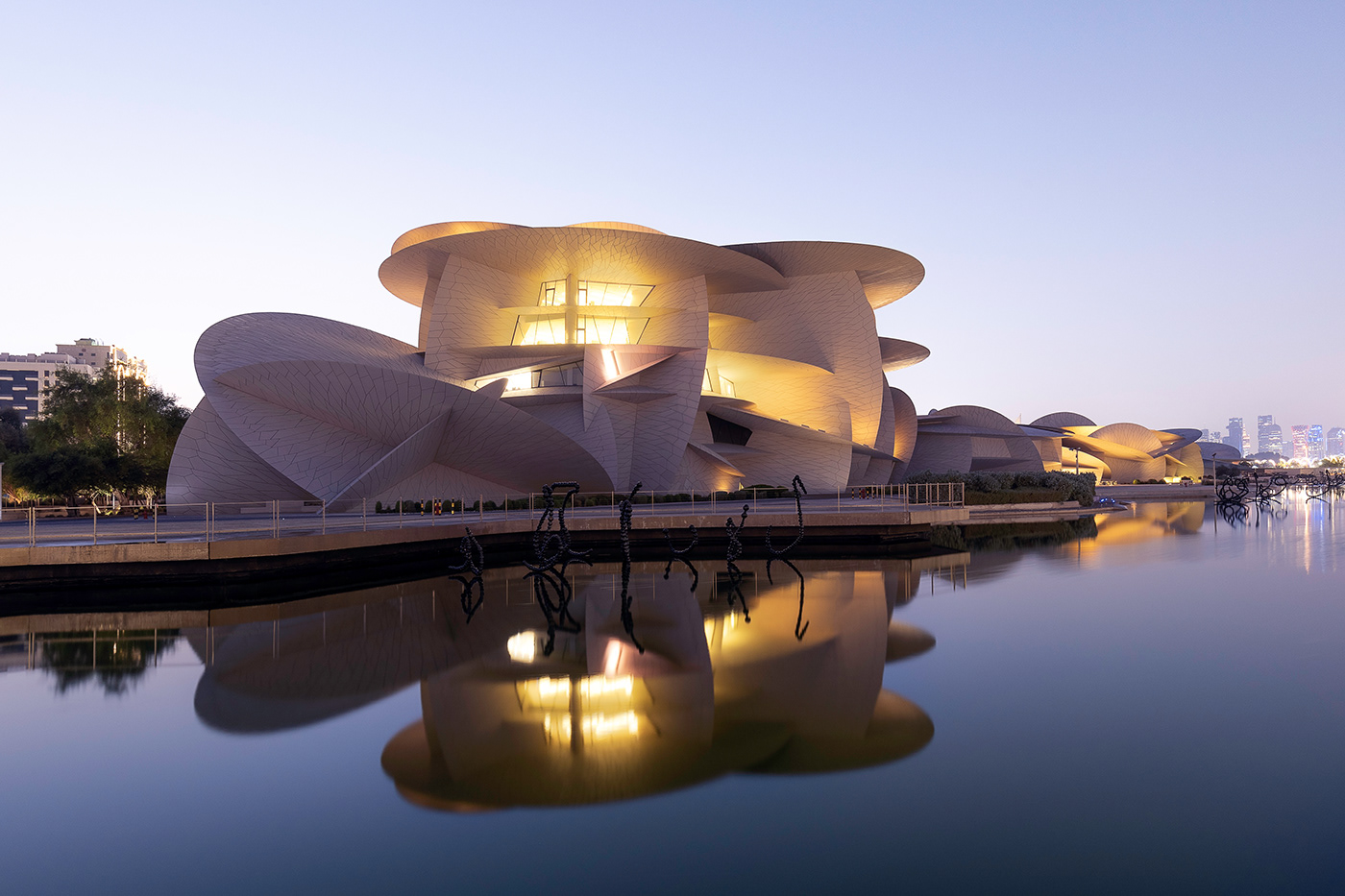 Museum of Qatar reflected in water, captured during the dusk with skyline of the Doha Corniche.