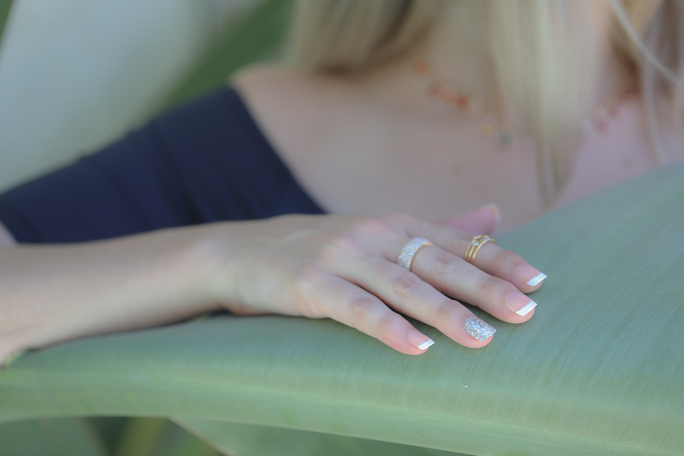 close up image of female manicured hand sitting on large green leaf with jewelry