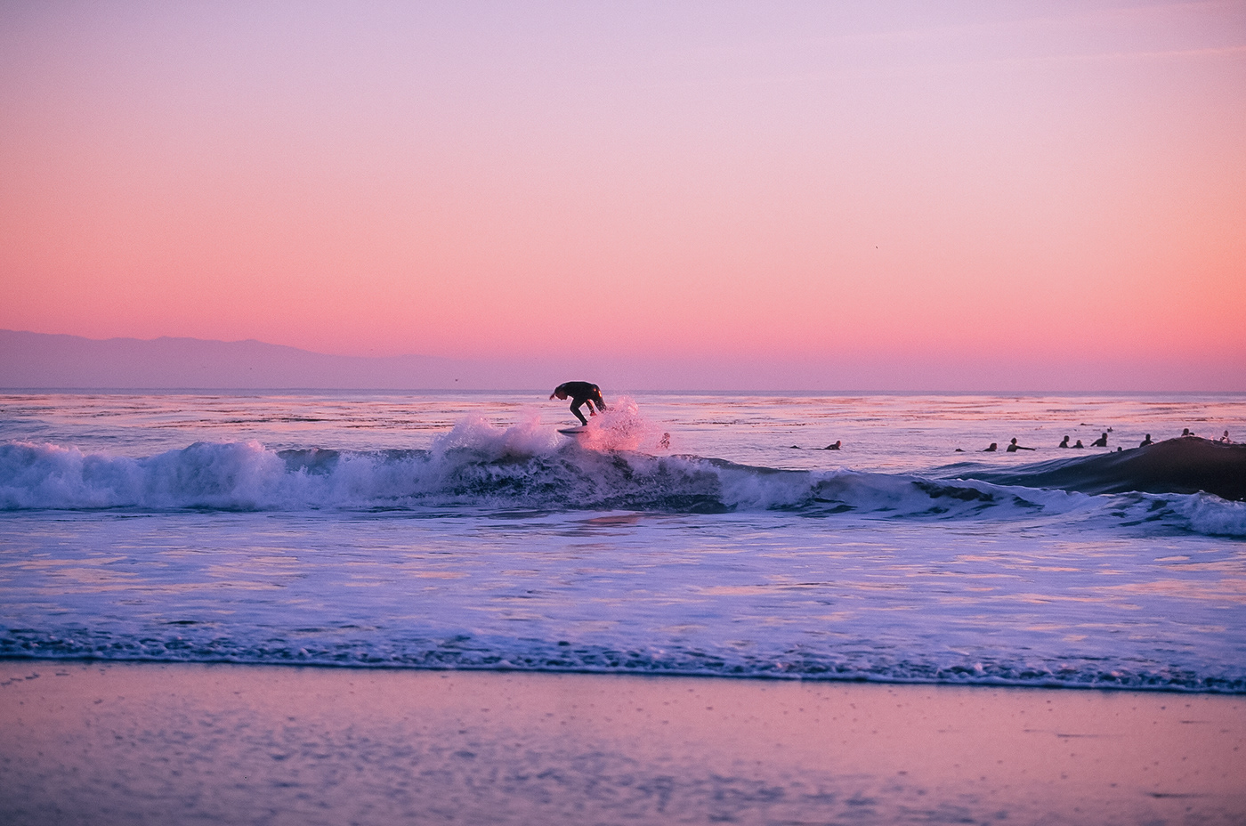 a surfer catches a pink wave at sunset
