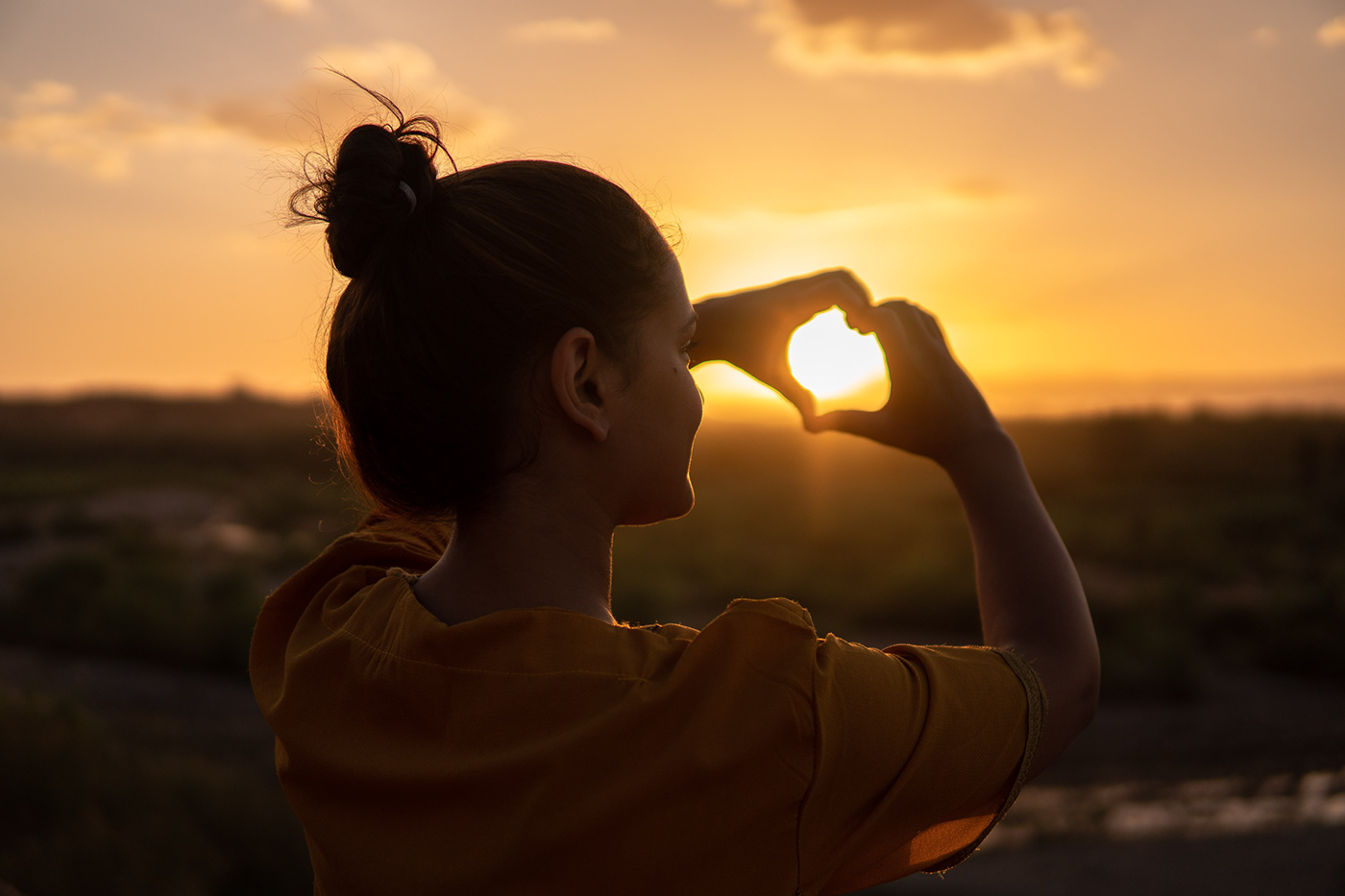 woman making a heart with her hands at sunrise