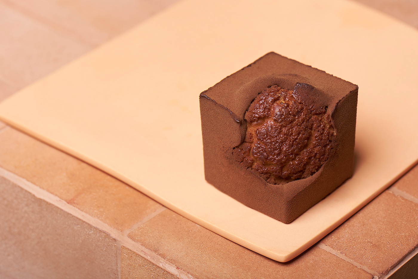 Photography of a chocolate cube cake on an orange ceramic plate. 