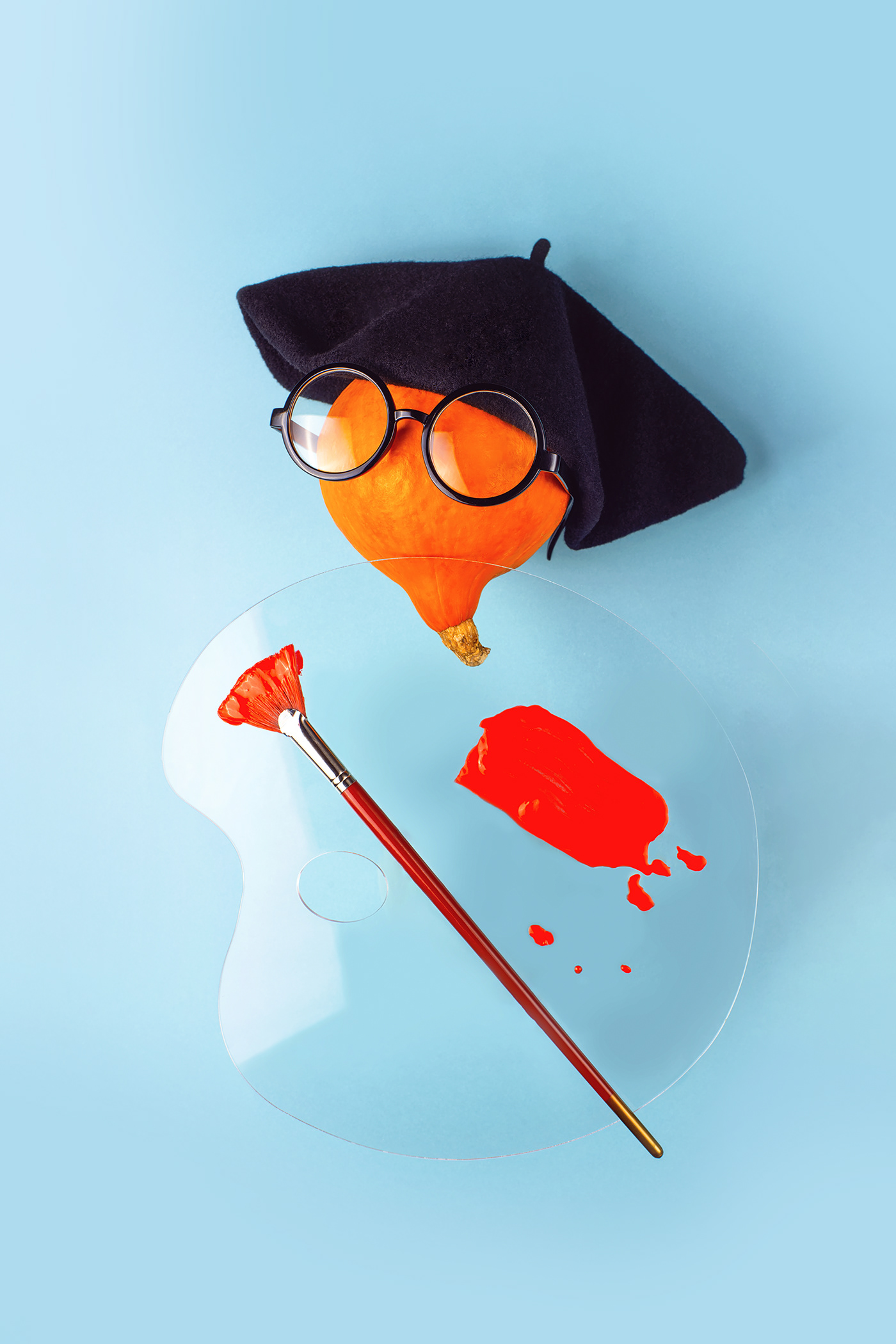 Orange decorative pumpkin artist in black beret, glasses, with a brush, palette and red paint 