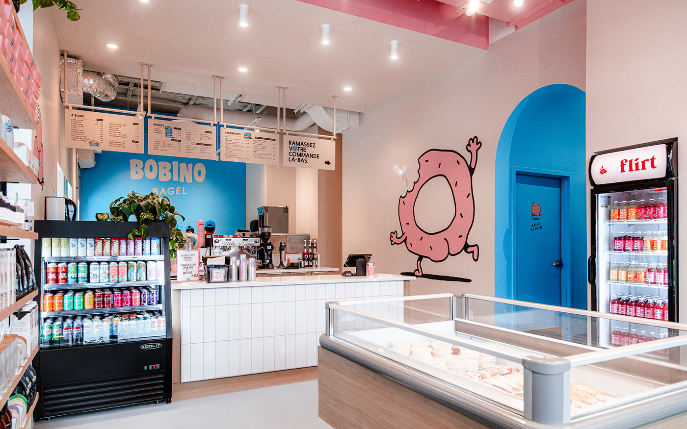 Cute bagel shop entry with a pink and blue walls. Large logo and wall art. Coffee and menu. Branded.