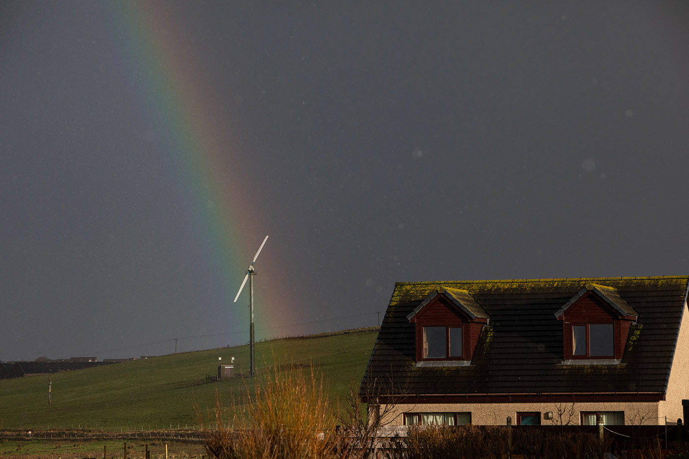 rainbow lands on a small wind turbines beside a home on a hillside