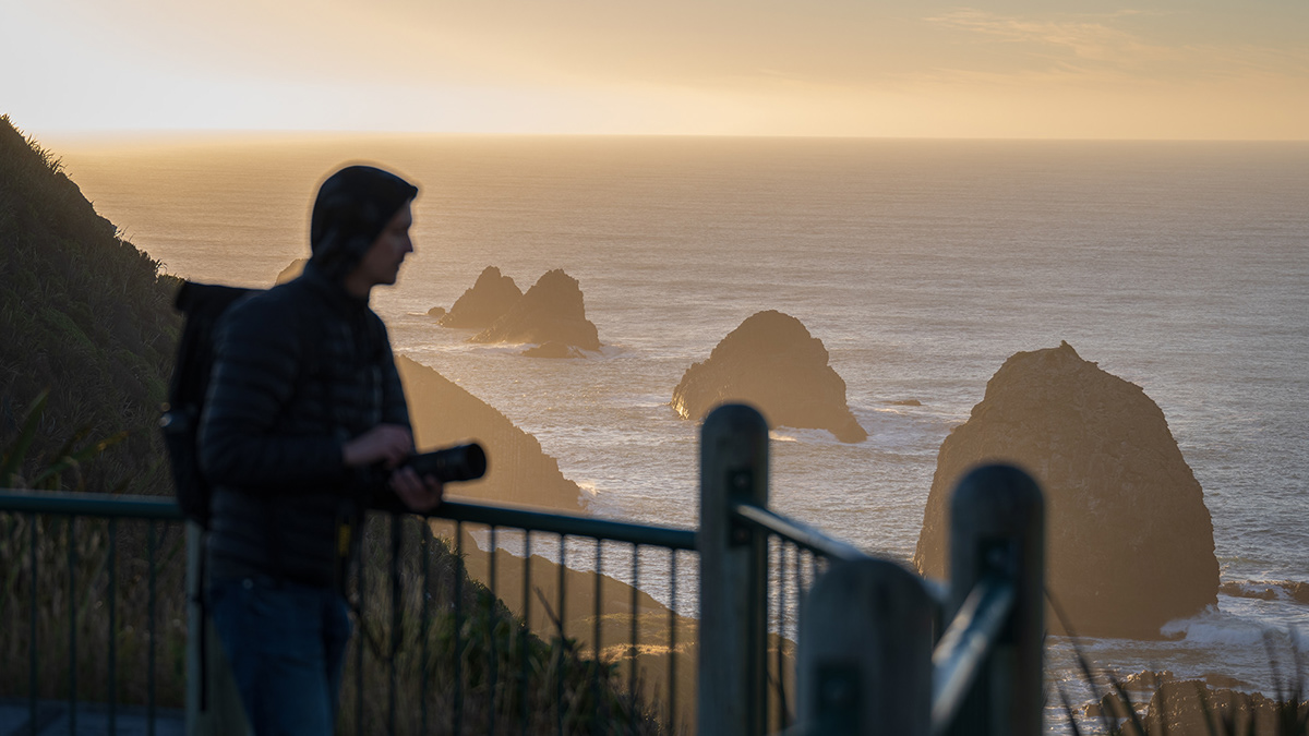 Silhouette of a person looking at the rock formations at Nugget Point being illuminated by the sun.