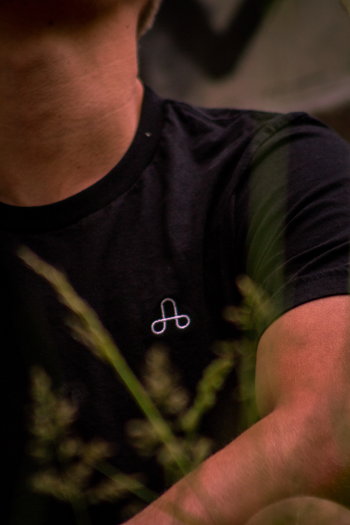 A close up shot of a model wearing The Uprising T-shirt focusing on the embroidered logo.