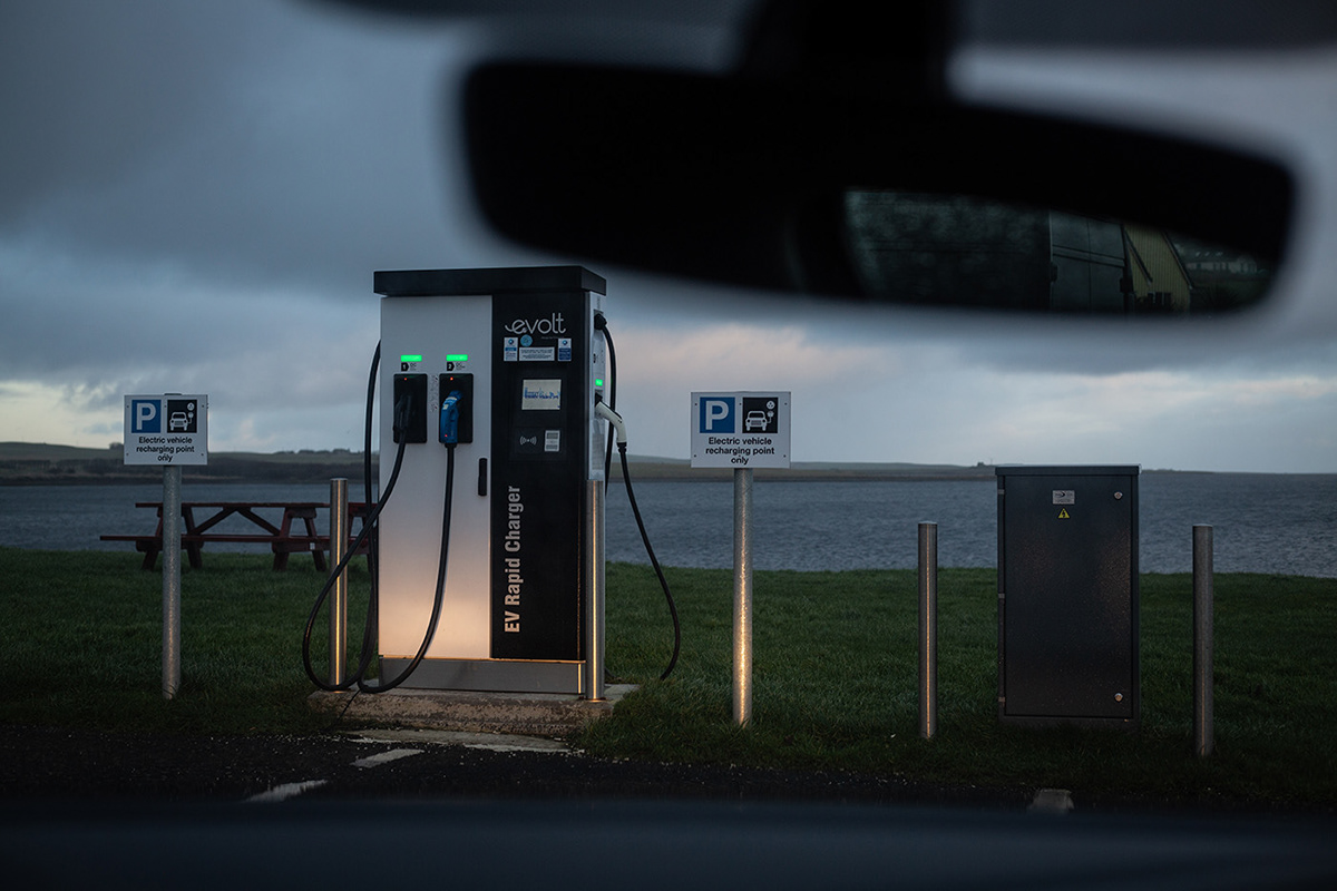 car electric charging point illuminated by car headlights, with loch behind