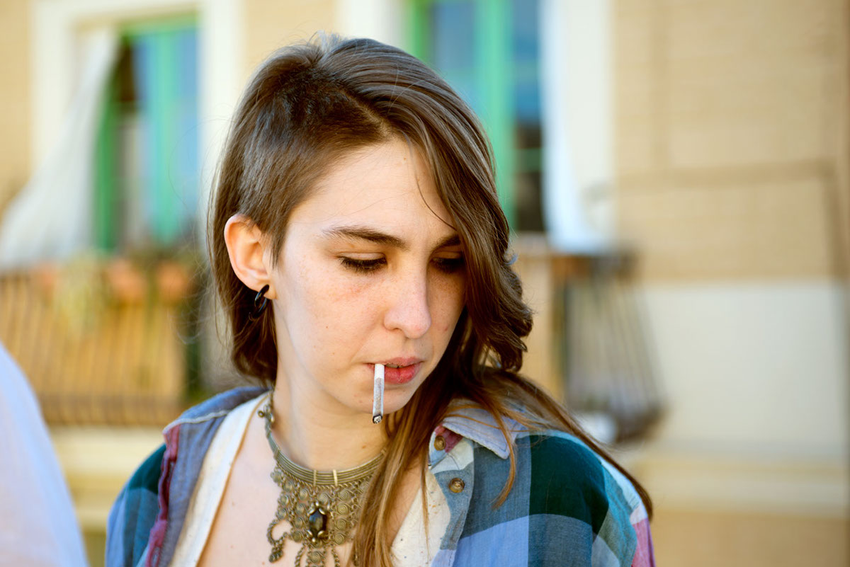 A woman with a joint in her mouth on an outdoor rooftop.