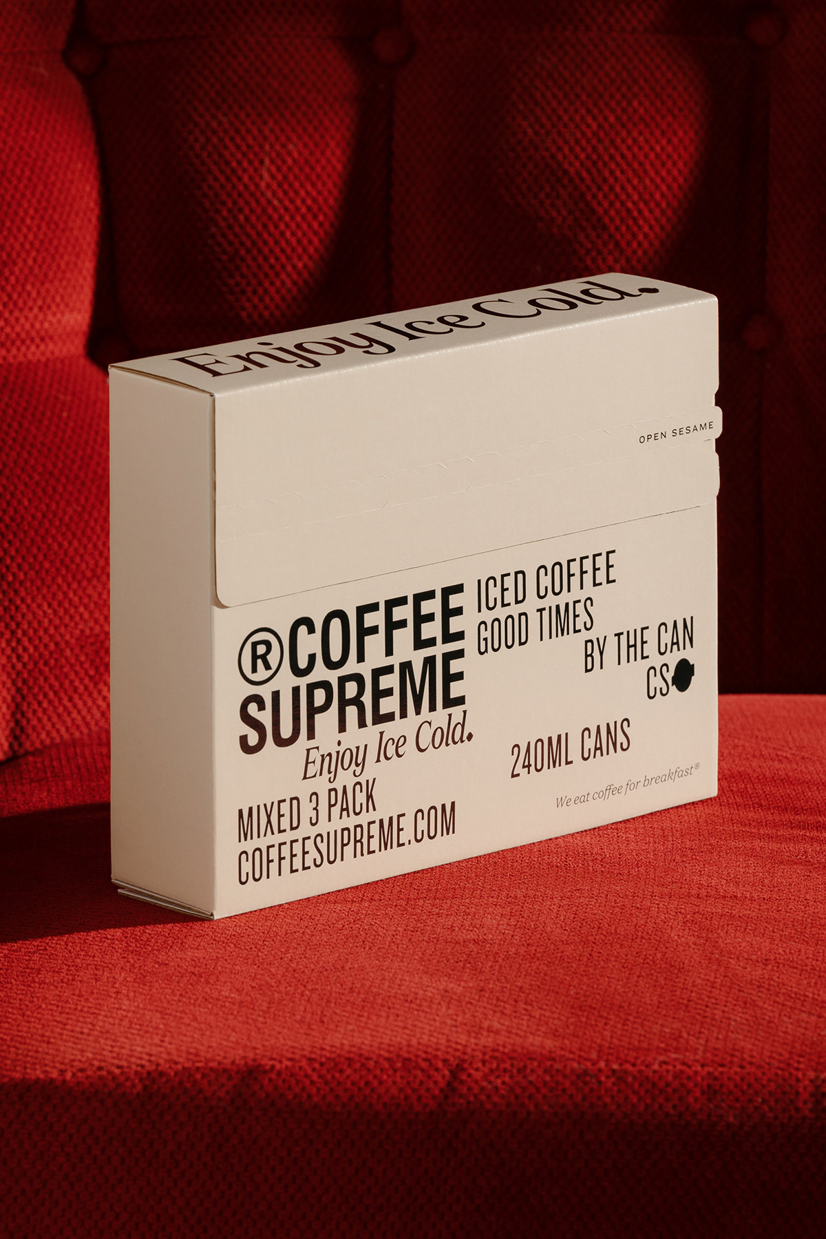 Black typography on a cream ecom mailer box sits on a red velvet couch