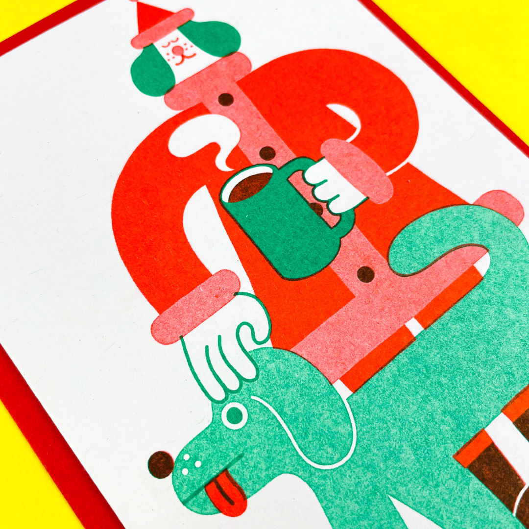Close up photo of a riso printed Xmas card. The design is of a dog dressed as Santa. 