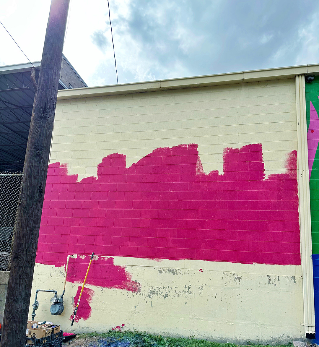 photo of large brick wall being painted bright pink background for a mural