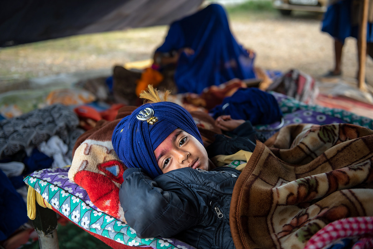 A young Nihang boy rests on a cot in a makeshift tent
