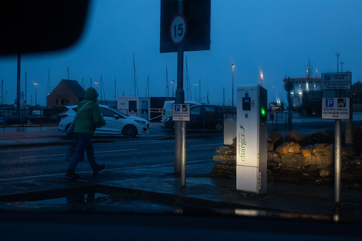cal electric charging point illuminated by car headlights, in blue light of dusk