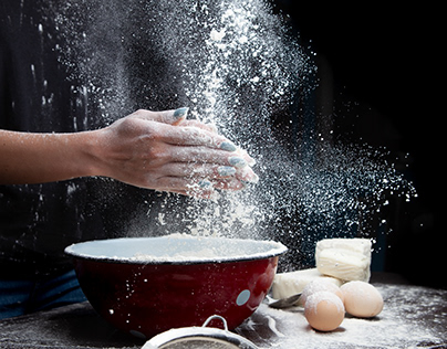 The chef sprinkles the flour on a dark background